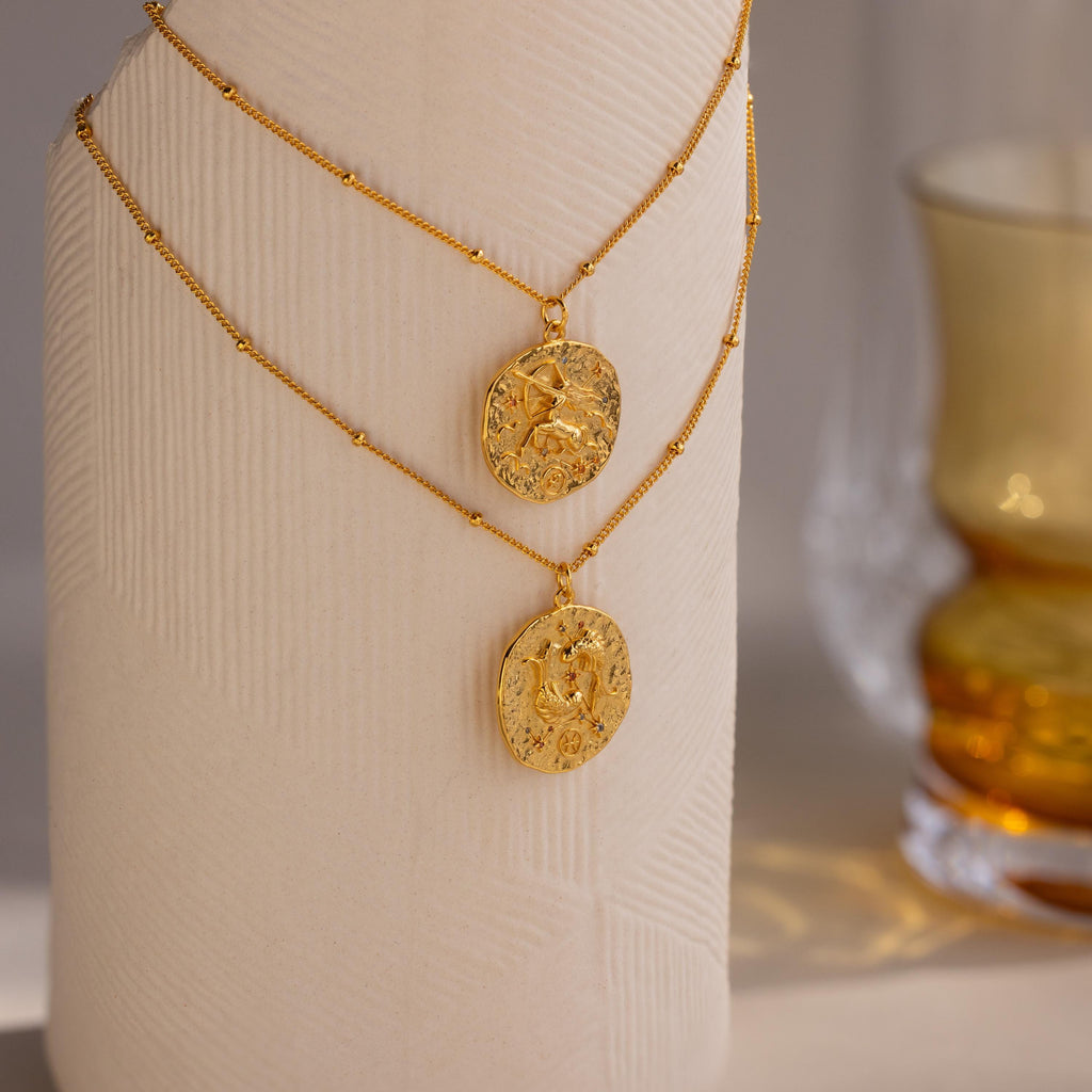 A Pisces and Sagittarius Zodiac Gemstone Coin Necklace hanging on a sculpture