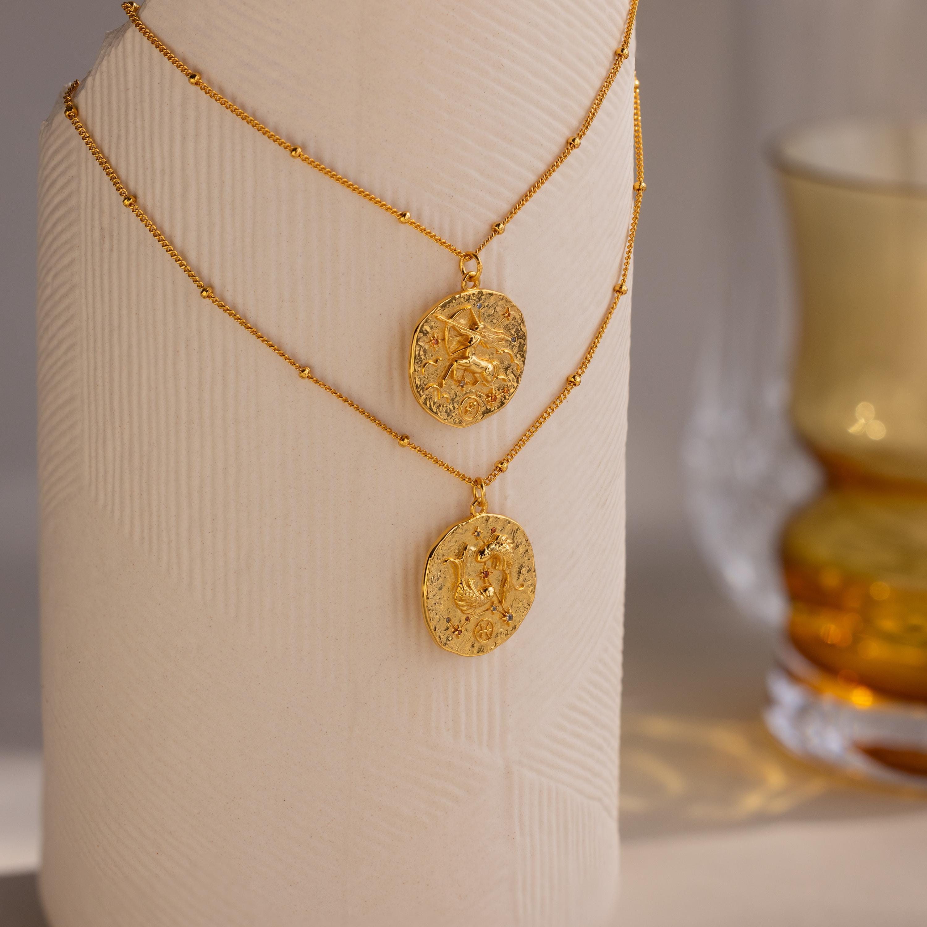 A Pisces and Sagittarius Zodiac Gemstone Coin Necklace hanging on a sculpture