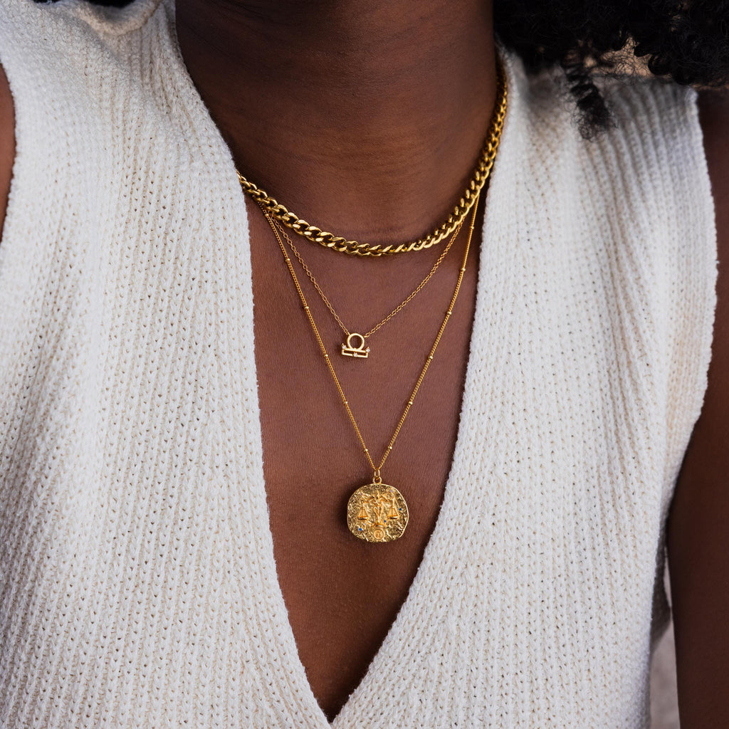 Model wears a gold libra Zodiac Gemstone Coin Necklace, pairing it with a libra symbol necklace and a gold curb chain