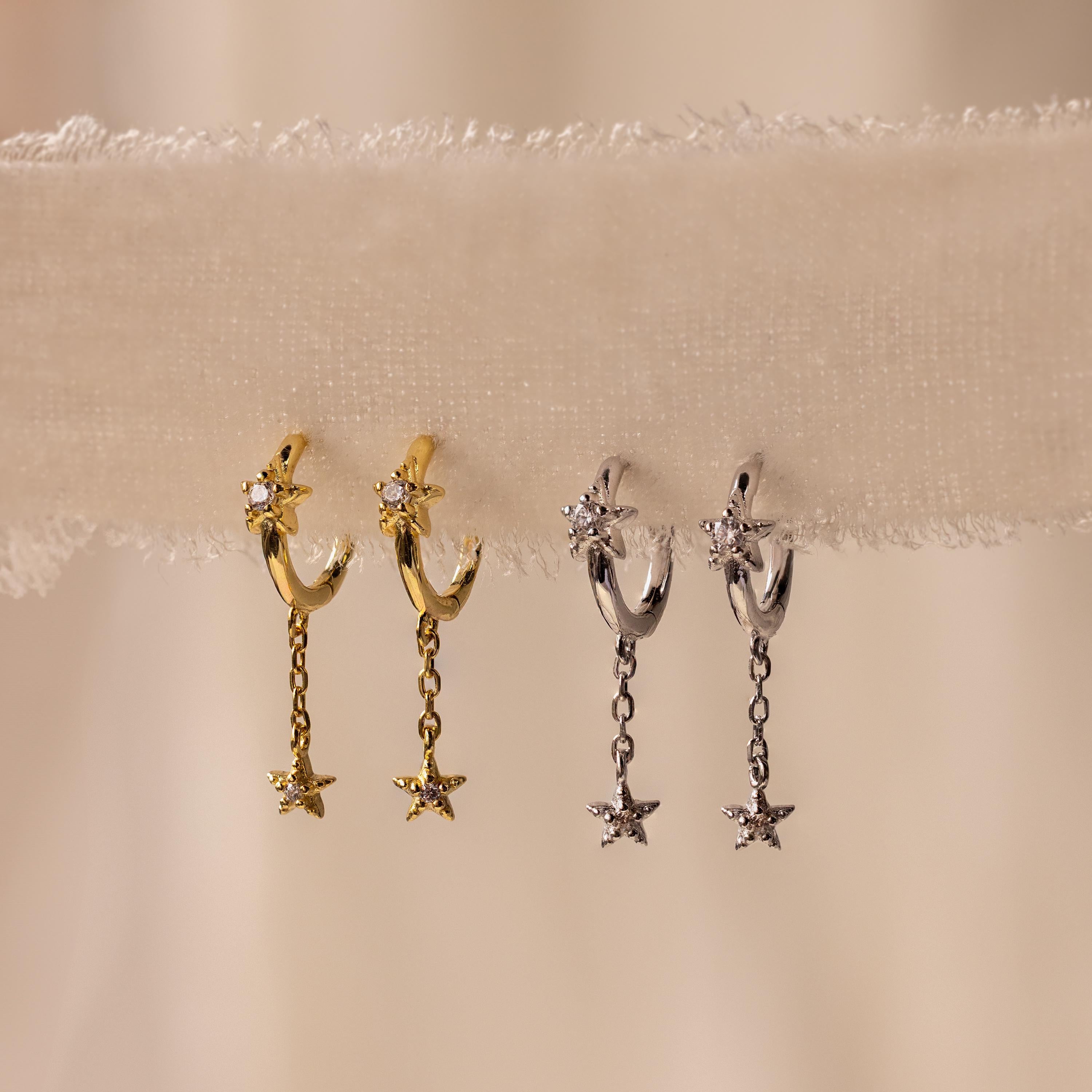 Gold and Silver Star Drop Chain Earrings hanging side by side on fabric