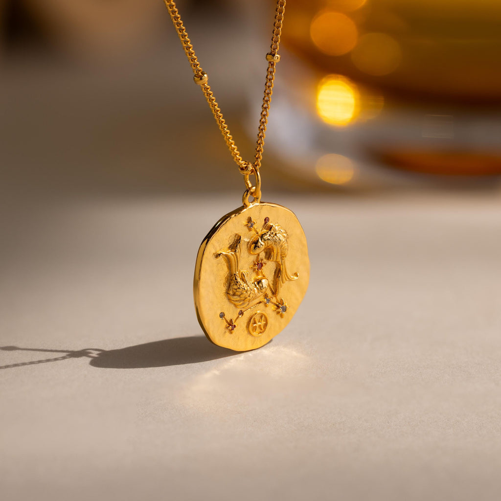Close up of a Gold 3D Pisces Zodiac Coin Pendant Necklace with small CZ gemstones, attached to a dainty satellite chain.