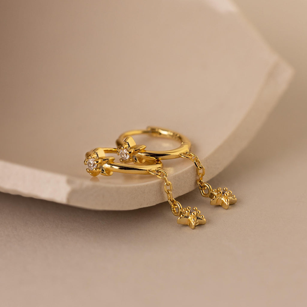 A pair of Gold Star Drop Chain Earrings laying side by side