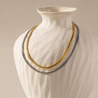 Two Foxtail Chain Necklaces—one in silver and one in 18K gold—layered on a matte white ceramic bust.