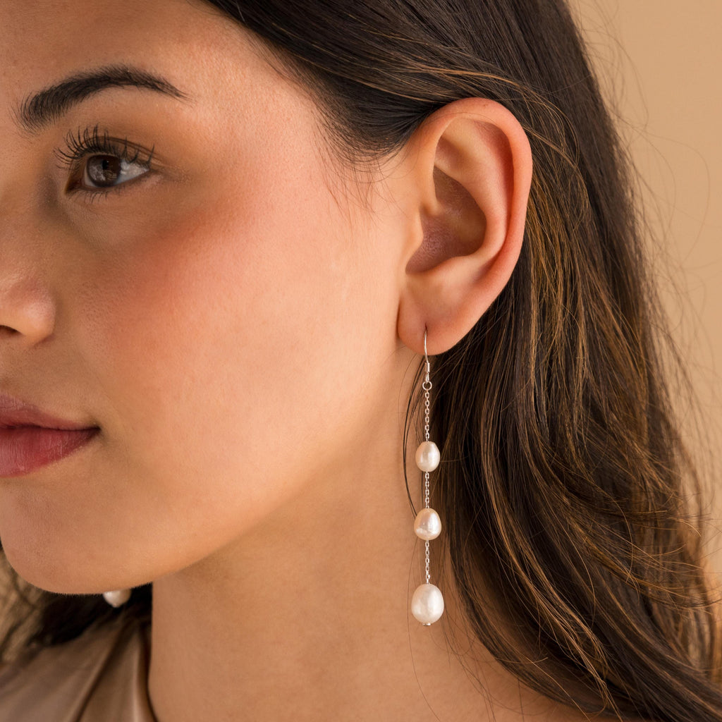 Close-up of model wearing long silver pearl chain earrings.