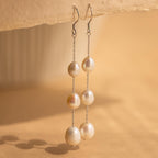 Close-up of a pair of long silver pearl chain earrings hanging from a tan surface.