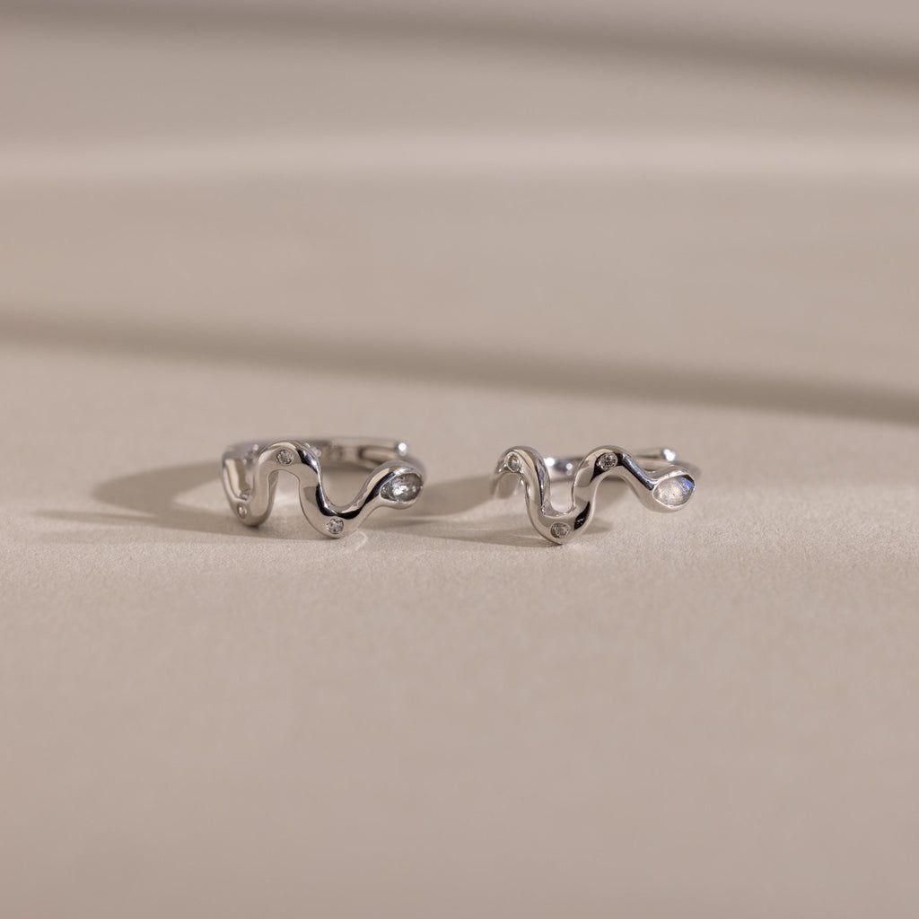 Silver Pavé Viper Huggie Earrings placed on a neutral-toned background