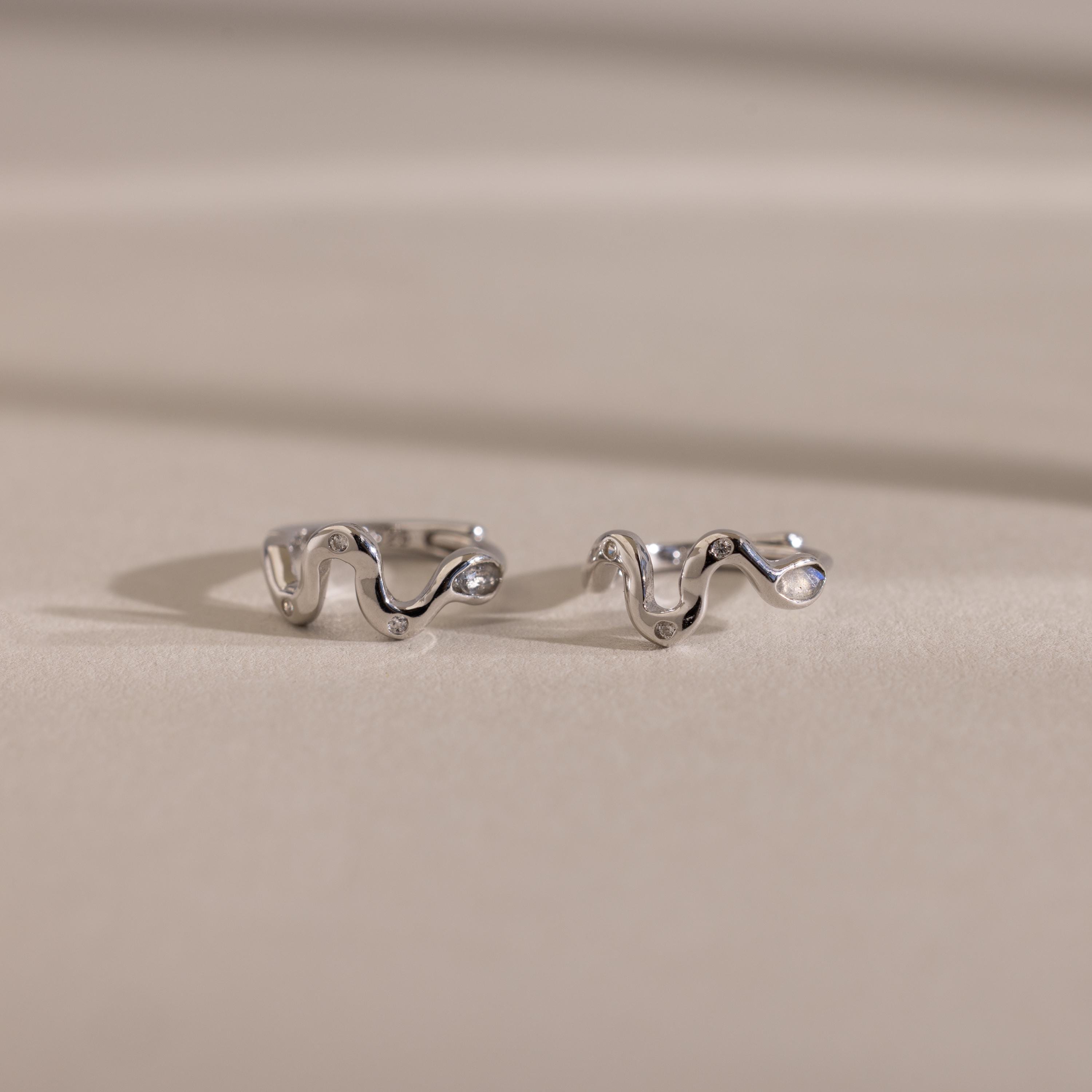 Silver Pavé Viper Huggie Earrings placed on a neutral-toned background