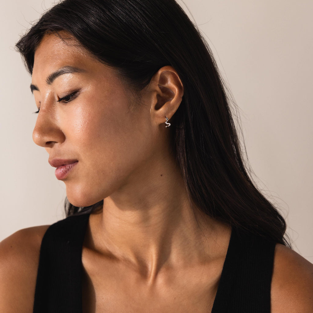 Model in profile view showcasing the silver version of the Pavé Viper Huggie Earrings
