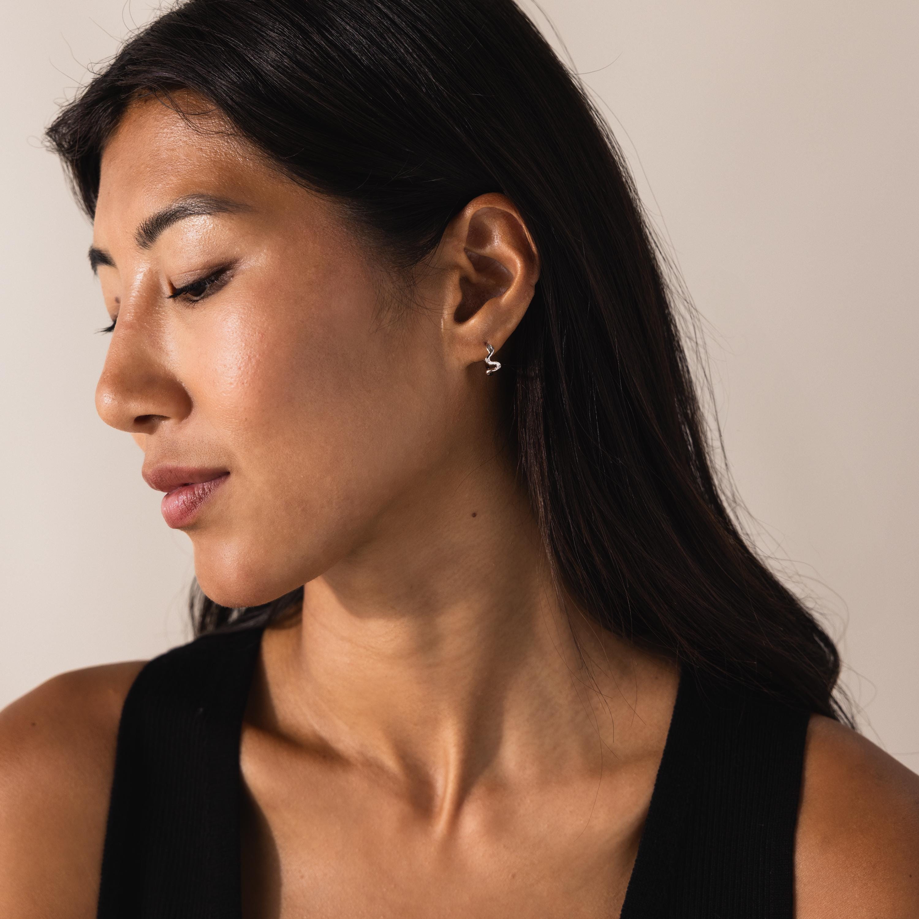 Model in profile view showcasing the silver version of the Pavé Viper Huggie Earrings