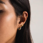 Close-up of a woman's ear wearing multiple gold earrings, including a small hoop, a stud, and sparkling Pave Viper Huggies.
