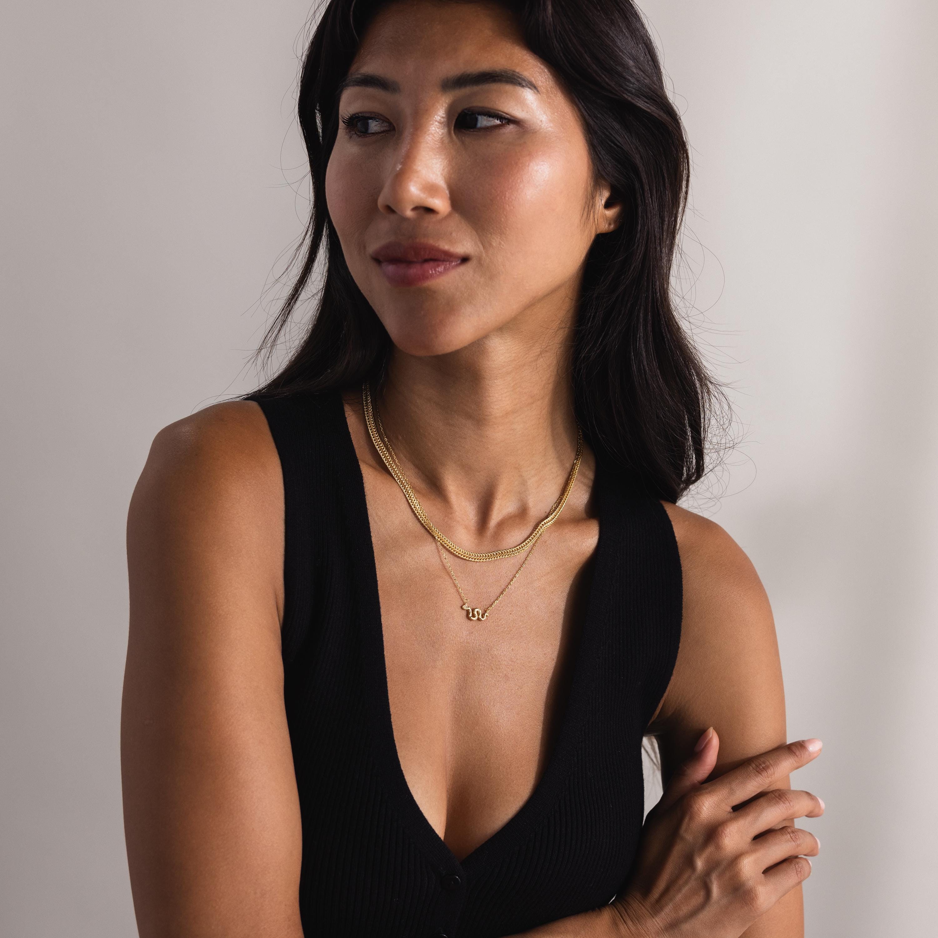 A woman wears the Thick Mesh Chain Necklace layered with a second delicate gold chain and a charm necklace