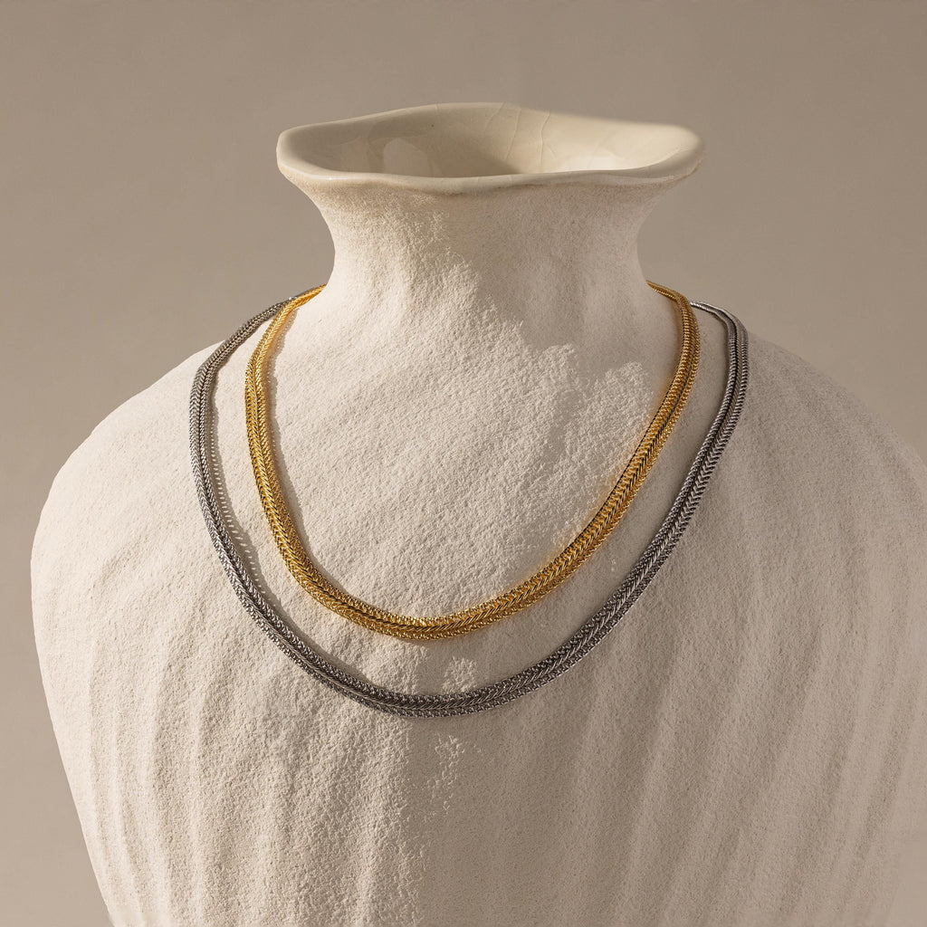 Flat lay of two Thick Mesh Chain Necklaces displayed on a sculptural ceramic bust—one in gold and the other in silver
