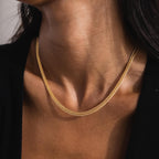 Woman wearing the Thick Mesh Chain Necklace in gold. The textured, wide mesh design features an intricate woven pattern, with a half curb chain design on top and a reversed curb chain side on the bottom, divided by a twisted border in the middle