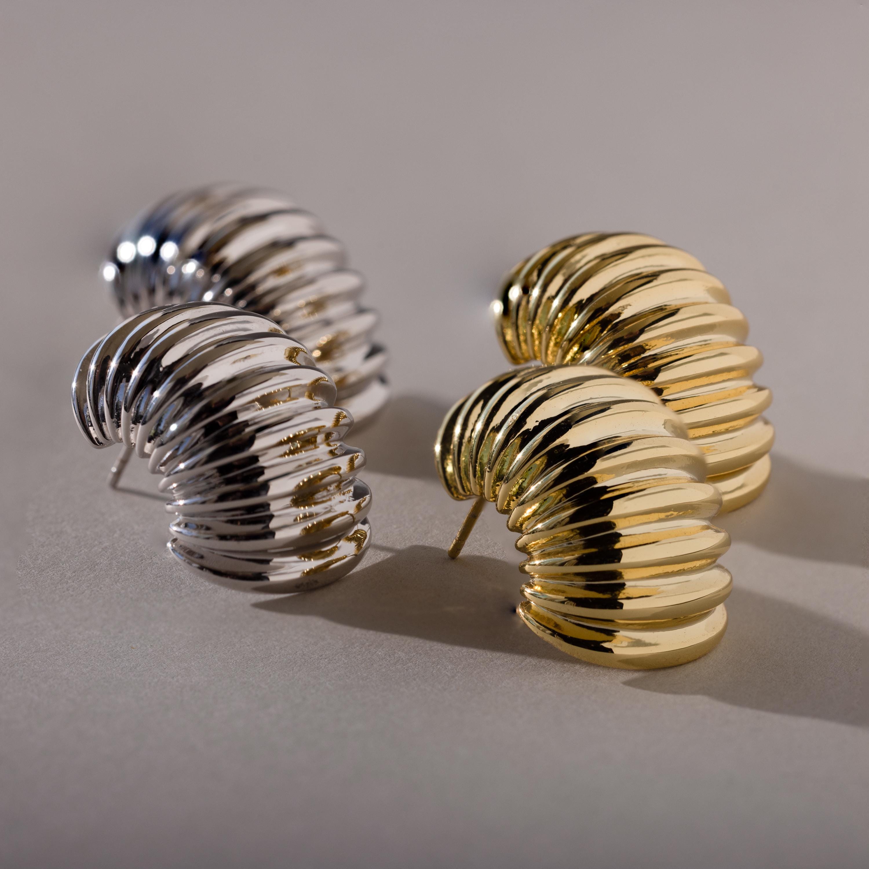 Flat lay of four earrings: two gold and two silver ribbed studs, arranged in pairs to display both finishes.
