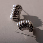 Silver ribbed huggie earrings arranged on a neutral surface