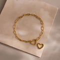 Heart Carabiner Paperclip Bracelet in gold laid flat with removable heart charm on a beige stone surface.
