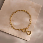 Heart Carabiner Paperclip Bracelet in gold laid flat with removable heart charm on a beige stone surface.