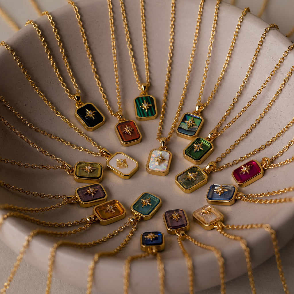 Gold chains with colorful, rectangular crystal pendants are arranged on a ceramic dish, showcasing the elegance of the North Star Opal Necklace.