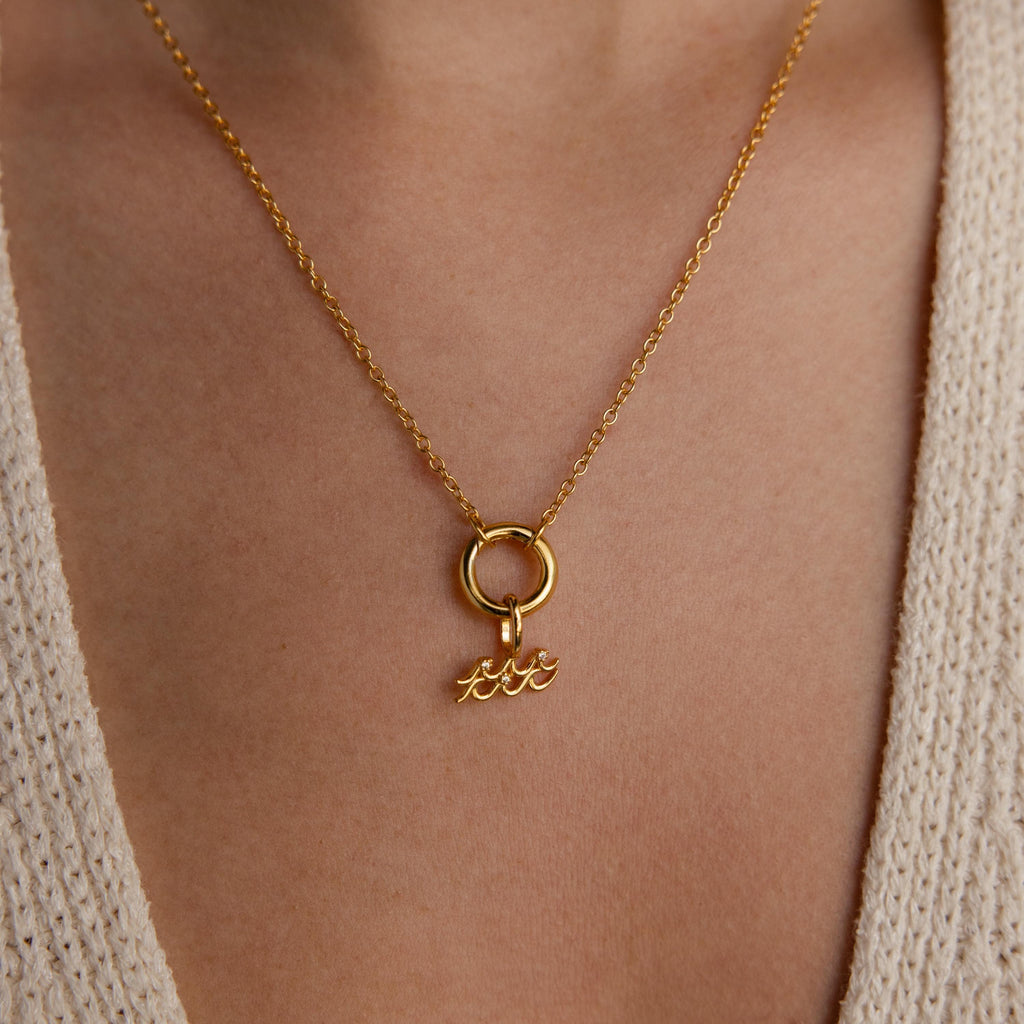 An Aquarius charm dangles from a circular bail on a gold chain, worn as a necklace.