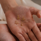 A hand holds four different gold zodiac charm pendants including Aquarius, Leo, Taurus, and Aries.