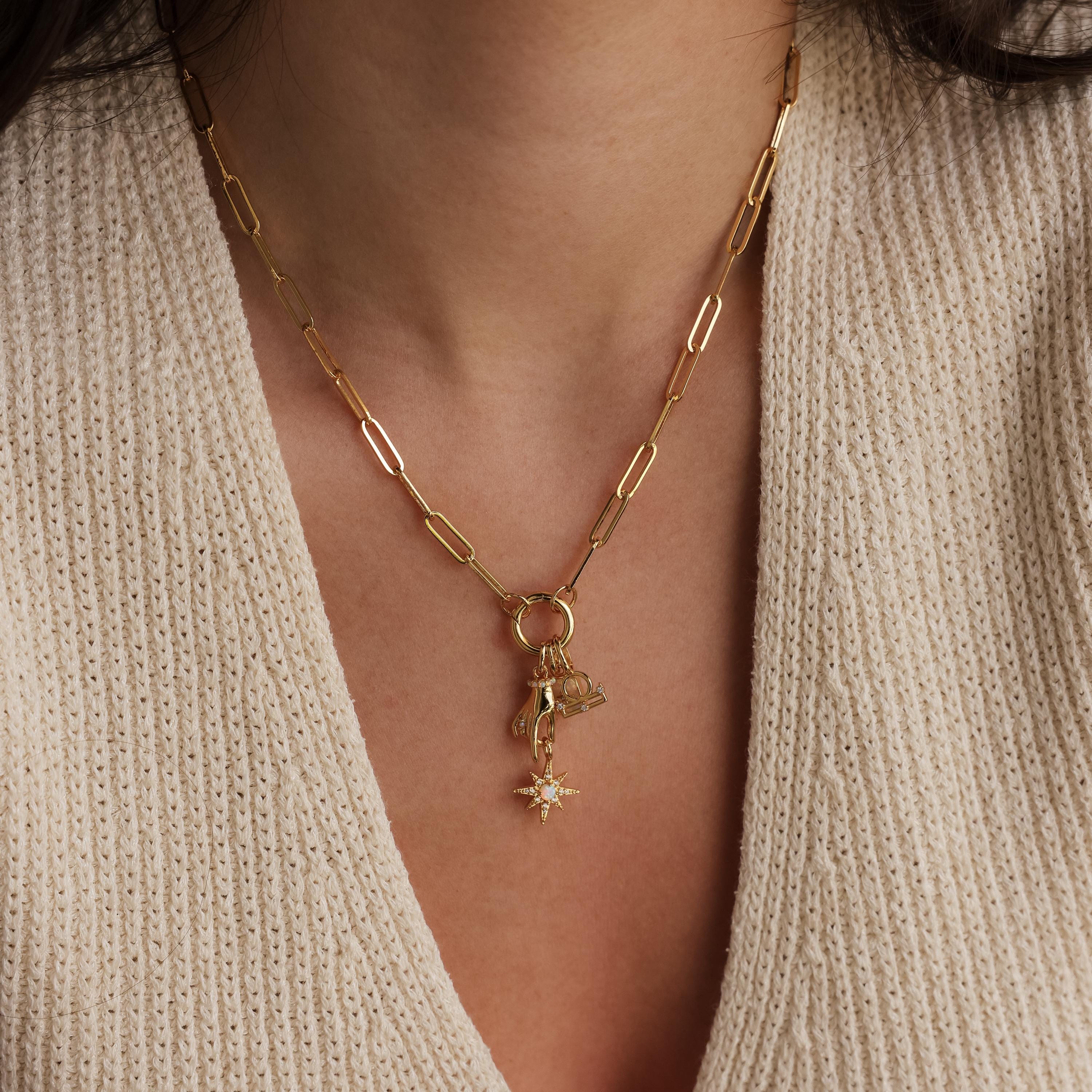 A model wears a gold paperclip chain necklace featuring a set of zodiac charms and a starburst pendant.