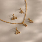 A flat-lay of gold zodiac charm pendants and a matching chain on a soft beige surface, featuring finely crafted zodiac symbols such as Aquarius, Libra, Gemini, Pisces, and others, each adorned with delicate cubic zirconia accents for subtle sparkle.