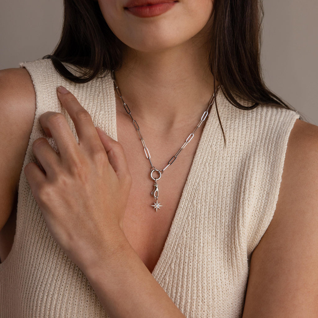 A silver version of the celestial hand and star pendant is worn on a silver paperclip chain necklace with a circular bail.