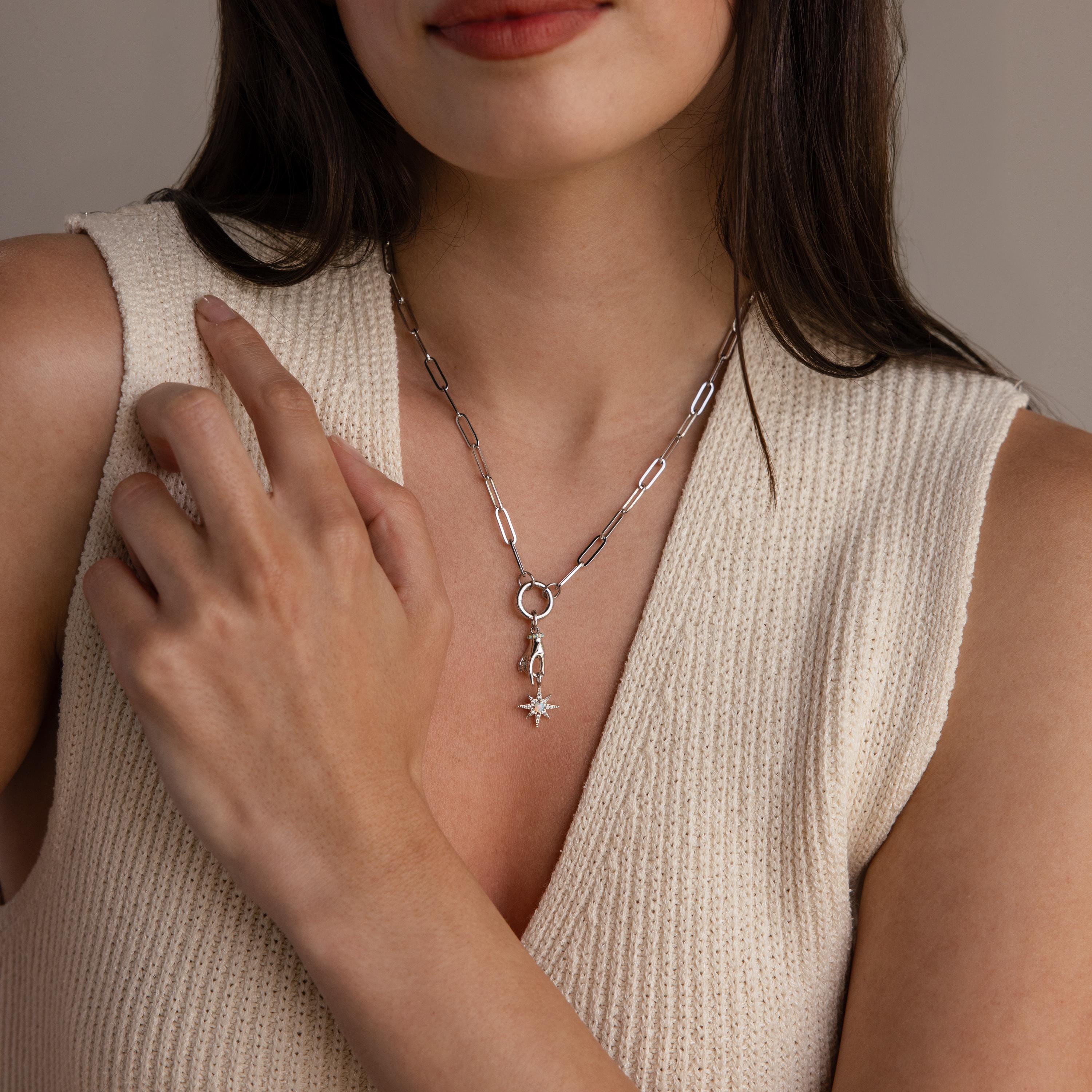 A silver version of the celestial hand and star pendant is worn on a silver paperclip chain necklace with a circular bail.