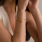 A woman in a sleeveless cream knit top wears the Heart Hand Charm gold bracelet, a symbol of affection.