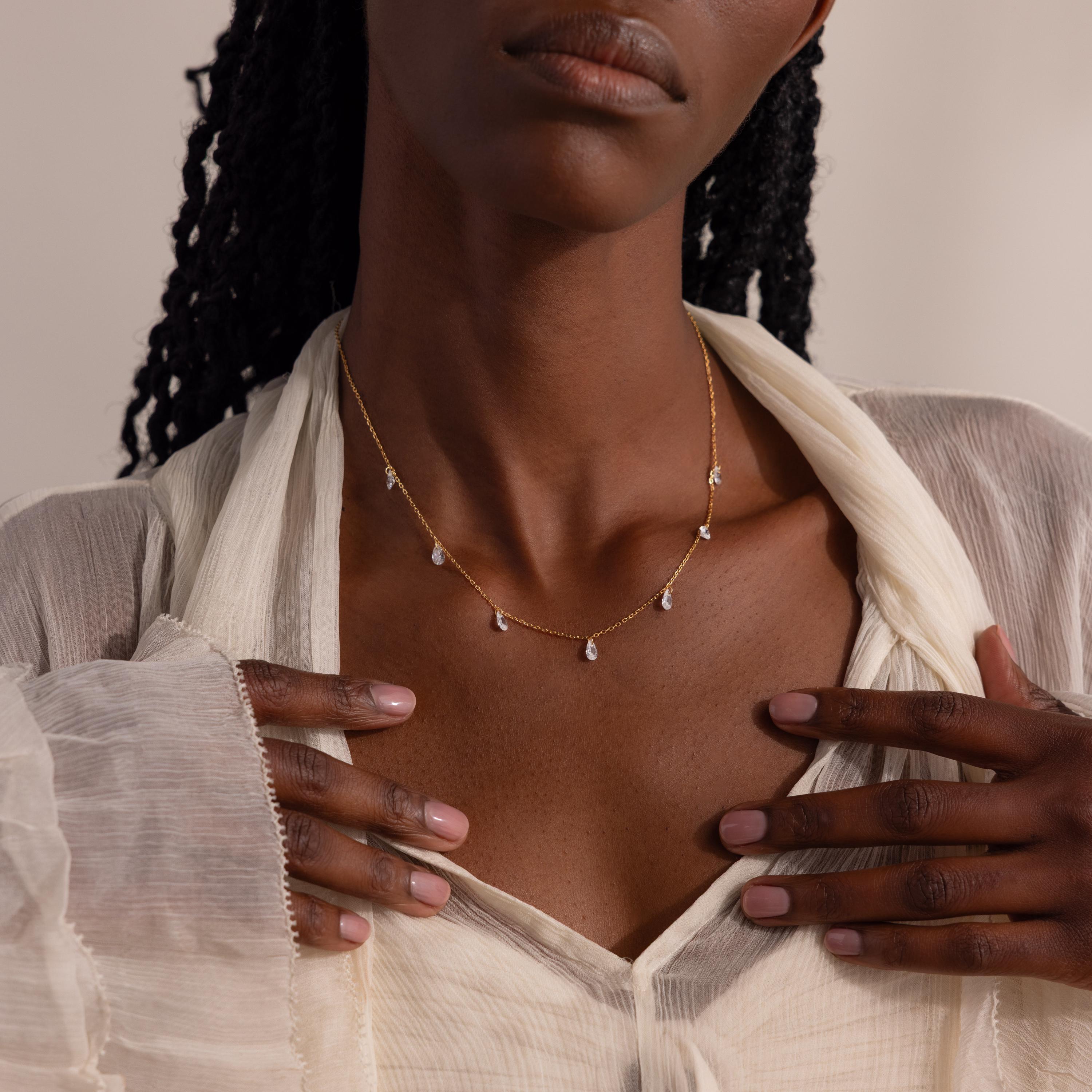 Model wearing the gold necklace with both hands gently framing it over a cream blouse.