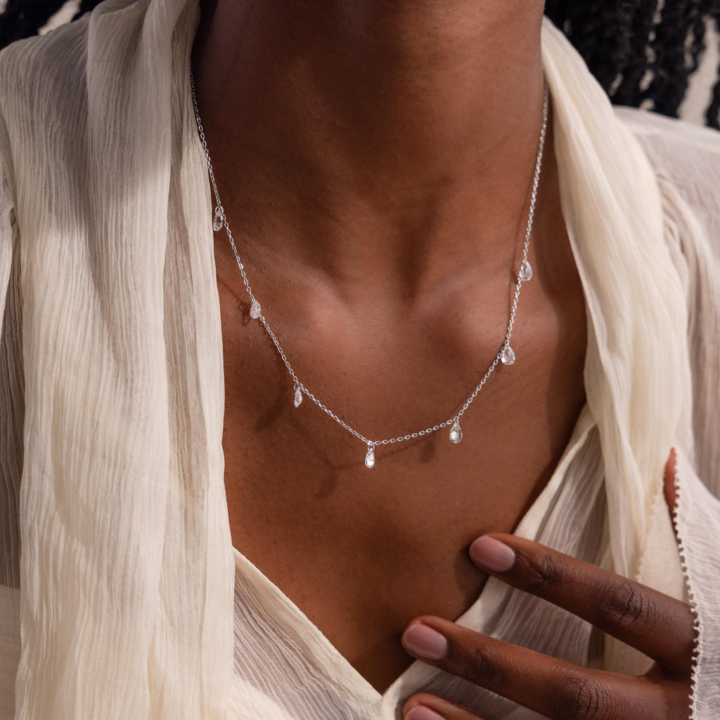 The same teardrop necklace in silver worn by a model with a neutral-toned blouse.