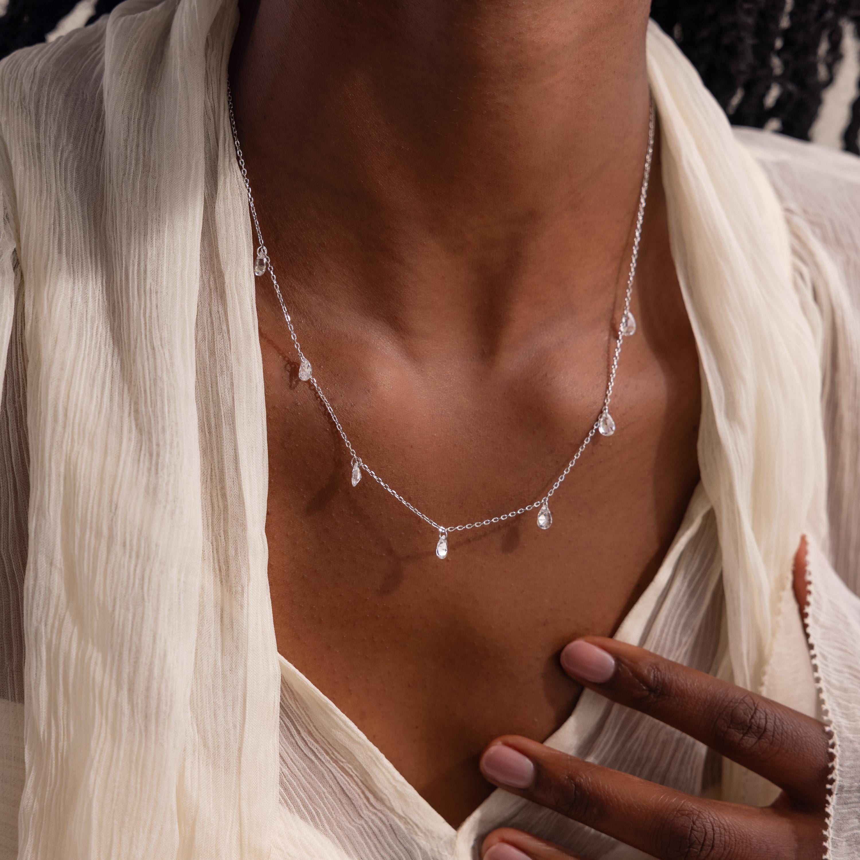 The same teardrop necklace in silver worn by a model with a neutral-toned blouse.