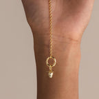A delicate gold rolo chain bracelet is held vertically, featuring a single dangling gold strawberry charm with sparkling crystal details.