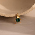 The Malachite Beetle Charm in gold lying upright, showing its vivid green wing casings and polished gold legs and crown.