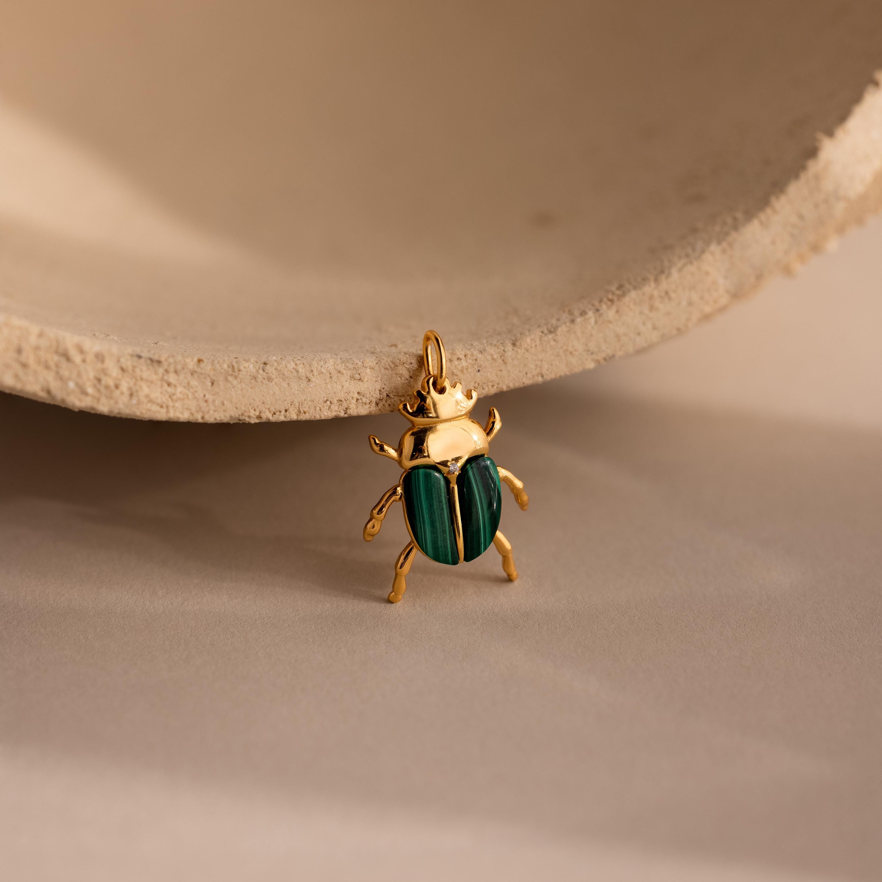 The Malachite Beetle Charm in gold lying upright, showing its vivid green wing casings and polished gold legs and crown.