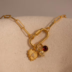 A gold Ribbed Heart Initial Pendant with a pavé letter is styled on a carabiner clasp link necklace alongside a strawberry charm and a red garnet gemstone charm