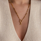 Model wearing a gold paperclip chain necklace with a single bubble letter “A” charm hanging from a Rolo Circle connector, styled over a beige knit top.