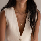 A woman models a minimalist gold chain necklace with a single Simple Heart Charm dangling at the center, styled simply over a deep V-neck blouse.