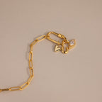 A flat-lay view of a gold paperclip chain featuring a carabiner lock and three attached charms: the Simple Heart Charm, a U-lock charm, and a pavé marquise charm.