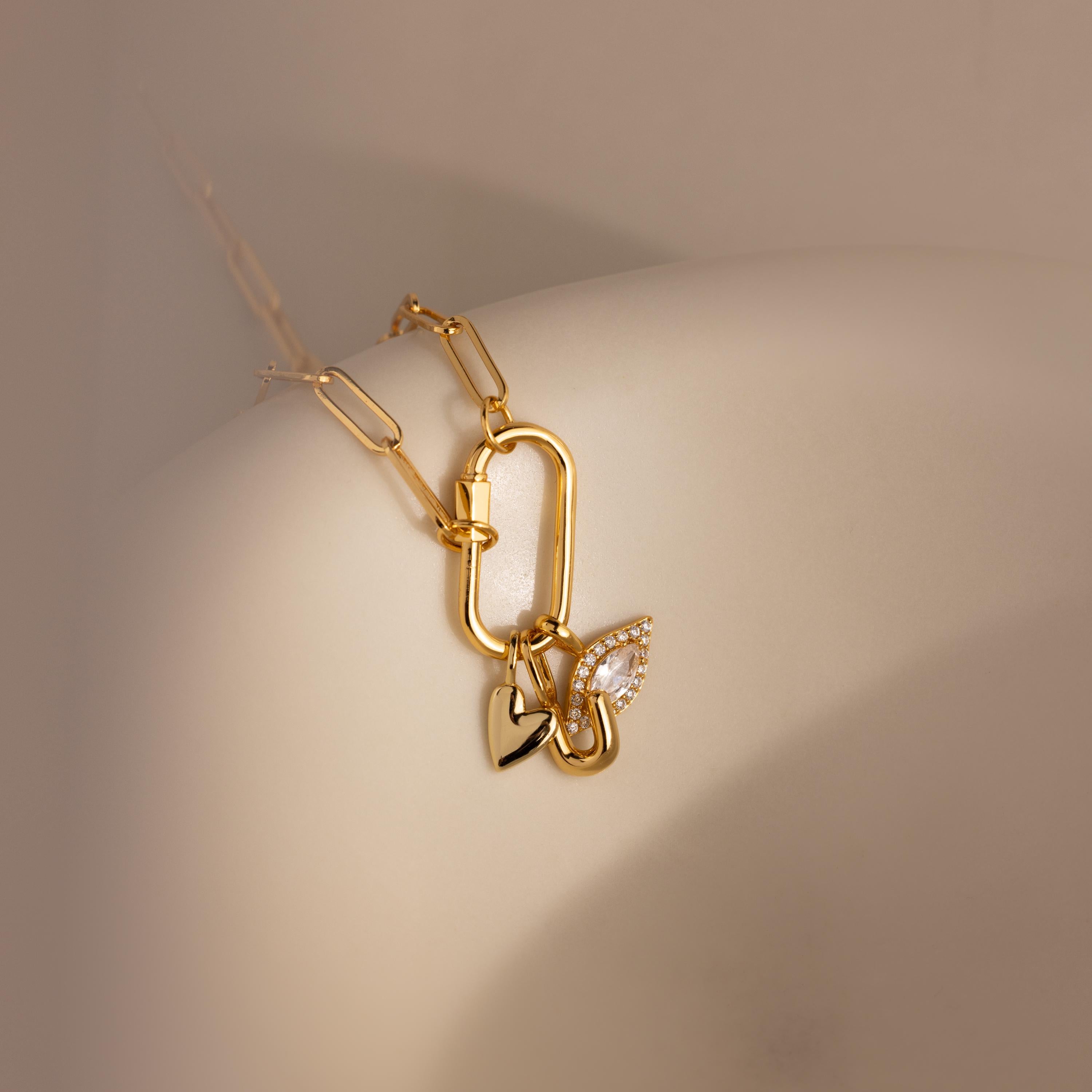 A detailed close-up of a necklace styled with three charms—including the Simple Heart Charm—hanging from a carabiner lock on a curved ceramic form.