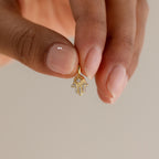 A hand holding up a single gold Evil Eye Hand Charm between two fingers, highlighting its small size and craftsmanship.