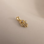 A close-up of the gold Evil Eye Hand Charm lying on a soft beige surface, showcasing its detailed stone-studded design.