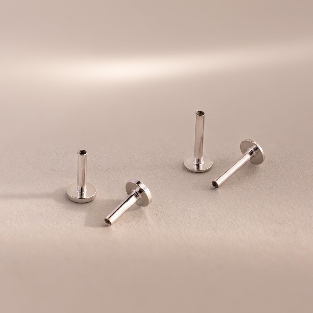 Four sterling silver Flat Back Posts in various upright and angled positions on a warm-toned surface.