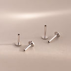 Four sterling silver Flat Back Posts in various upright and angled positions on a warm-toned surface.