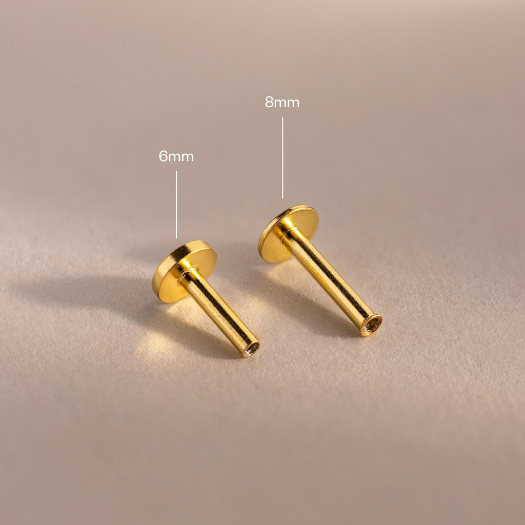 Close-up of two 18k gold Flat Back Posts lying down, showcasing the smooth finish and hollow post detail.