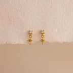 A straight-on product display of the 18k gold Diamond Star Flatback Earrings against a soft beige and off-white background, highlighting the charm's clean symmetry.