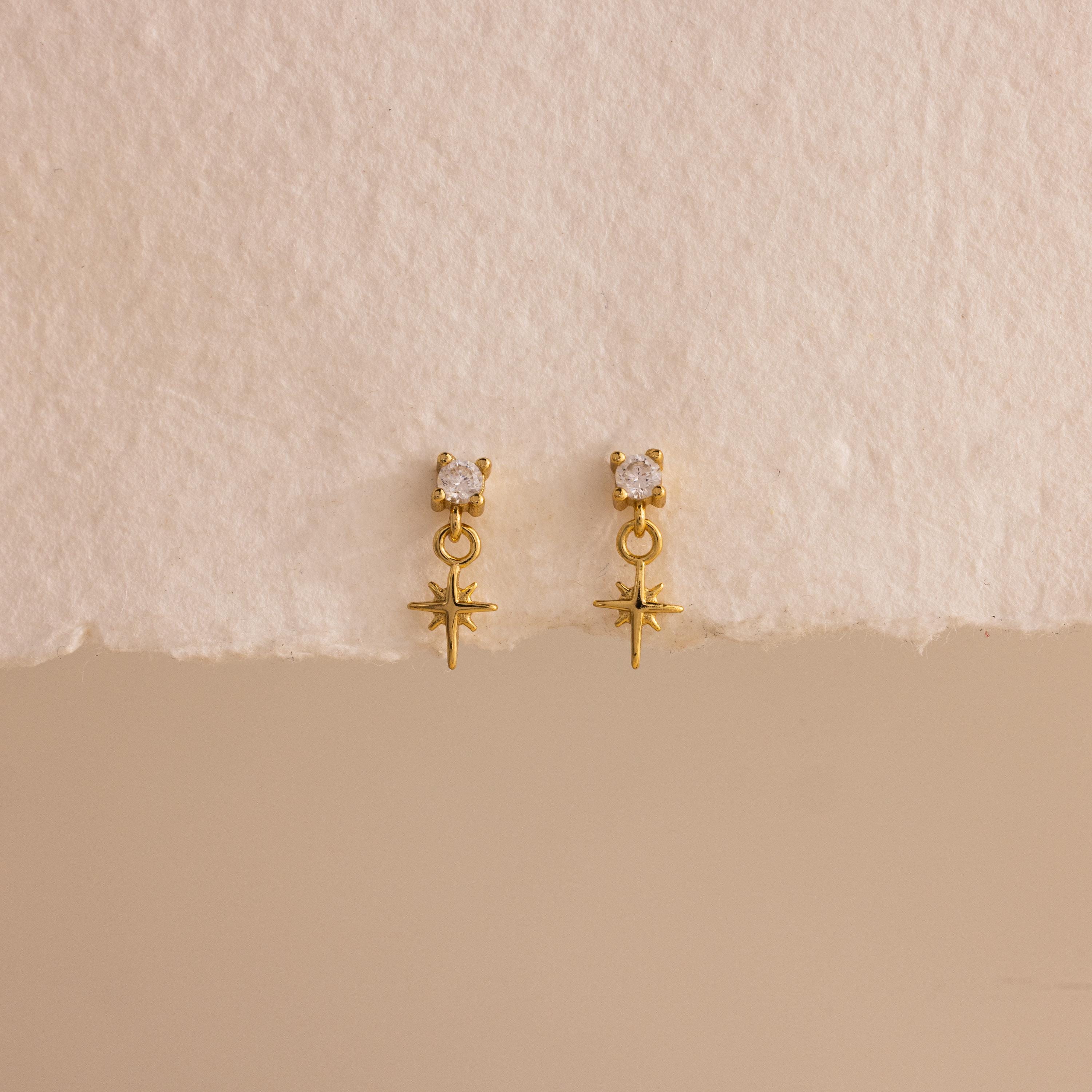 A straight-on product display of the 18k gold Diamond Star Flatback Earrings against a soft beige and off-white background, highlighting the charm's clean symmetry.