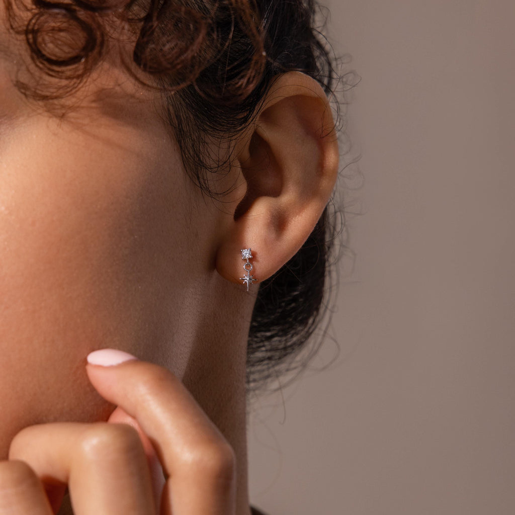 Close-up of a woman wearing a silver flatback earring featuring a small diamond stud and a delicate dangling star charm.
