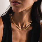 Close-up shot of a woman wearing a Foxtail Chain Necklace in 18K gold. The necklace rests elegantly along the base of her neck, showcasing its tightly interwoven, double-link design characteristic of the foxtail chain pattern.