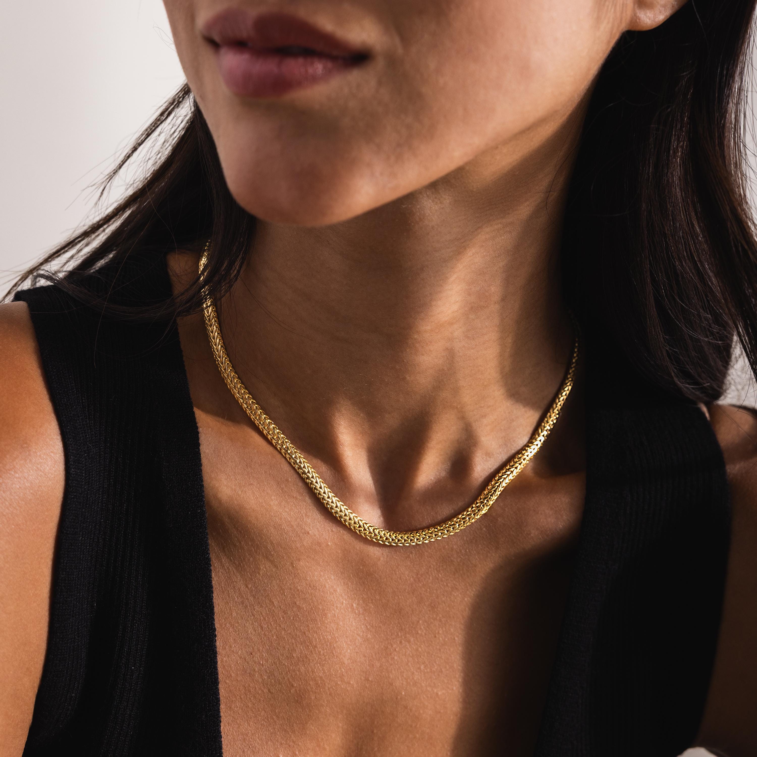 Close-up shot of a woman wearing a Foxtail Chain Necklace in 18K gold. The necklace rests elegantly along the base of her neck, showcasing its tightly interwoven, double-link design characteristic of the foxtail chain pattern.
